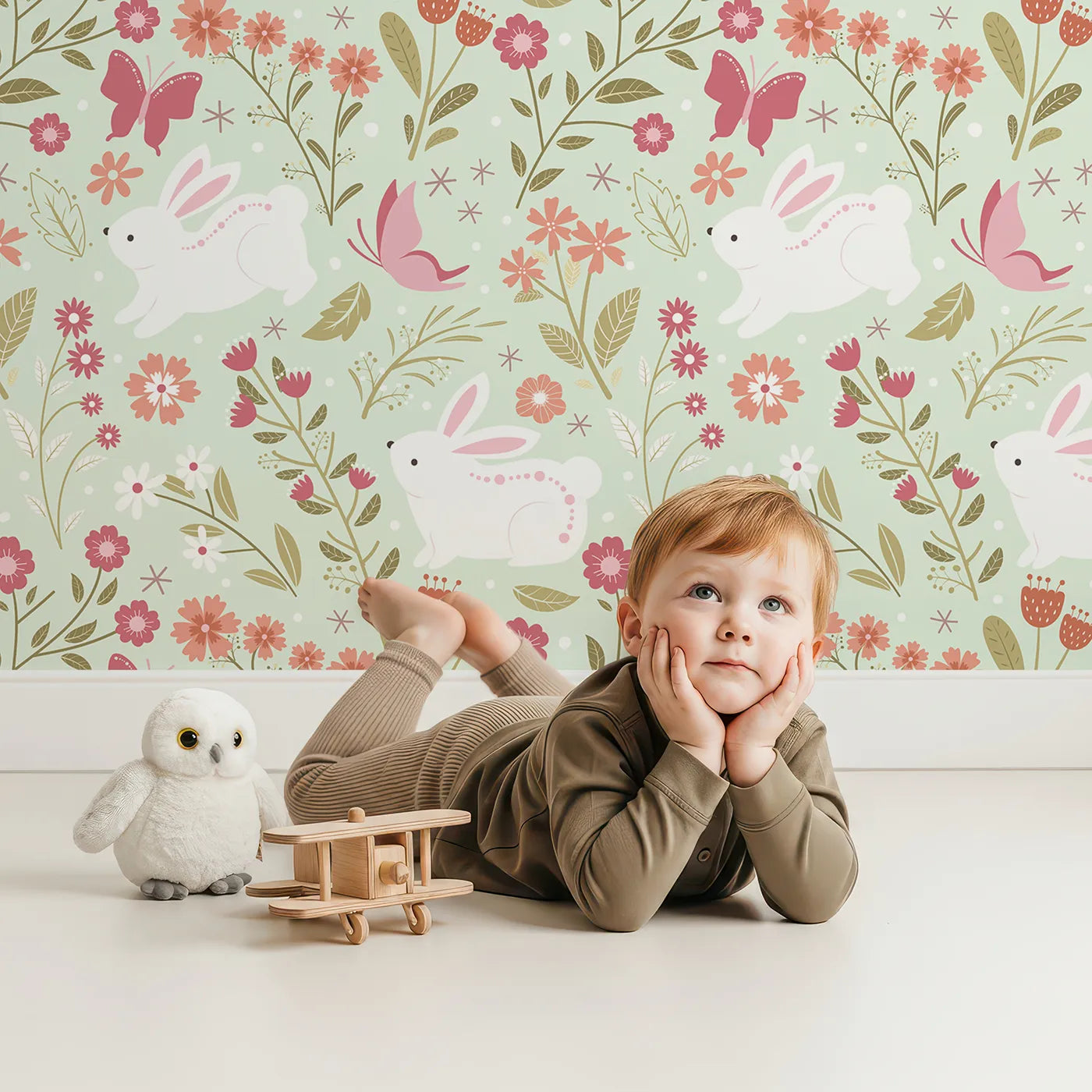 Lovely child standing in front of Whimsy Tots Meadow Hops Bunny Wallpaper in Mint Green with rabbit, butterfly, flower, leaf in design.