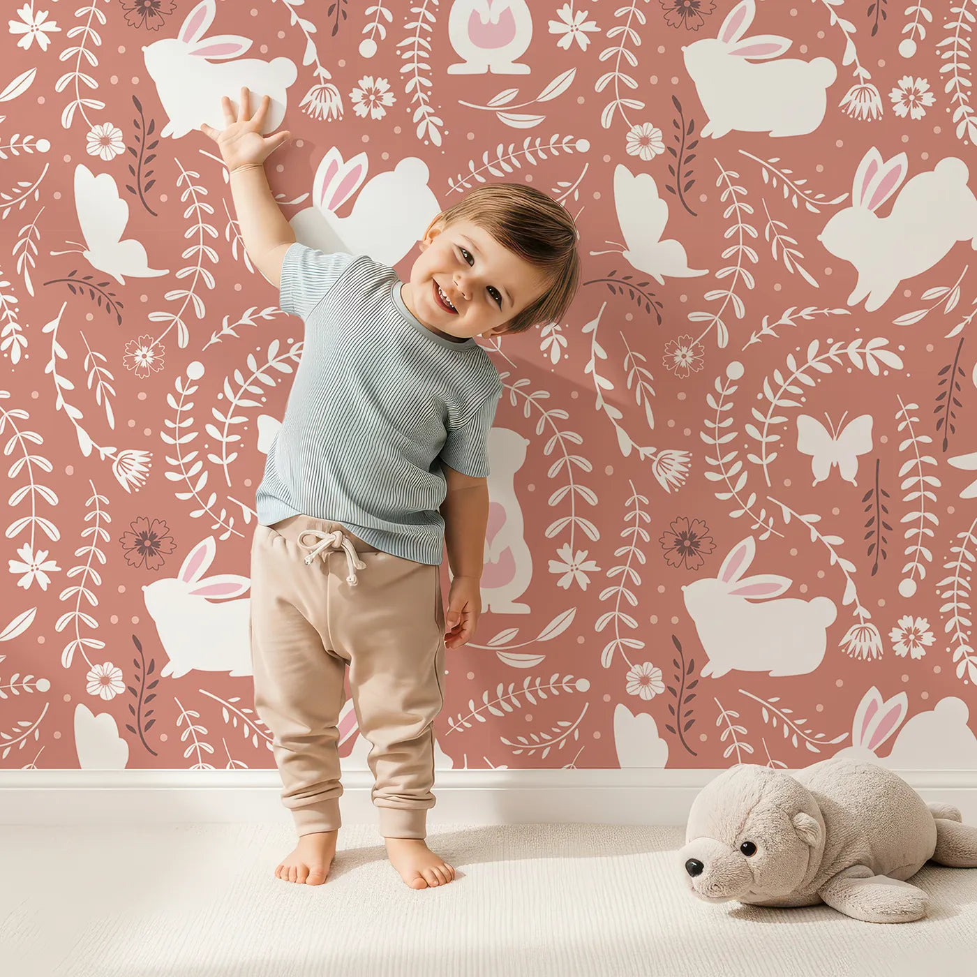 Lovely child standing in front of Whimsy Tots Bunny Hideaway Meadow Wallpaper in Terracotta Brown with rabbit, butterfly, flower, vine in design.