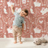 Lovely child standing in front of Whimsy Tots Bunny Hideaway Meadow Wallpaper in Terracotta Brown with rabbit, butterfly, flower, vine in design. Lovely child standing in front of Whimsy Tots Bunny Hideaway Meadow Wallpaper in Terracotta Brown with rabbit, butterfly, flower, vine in design.