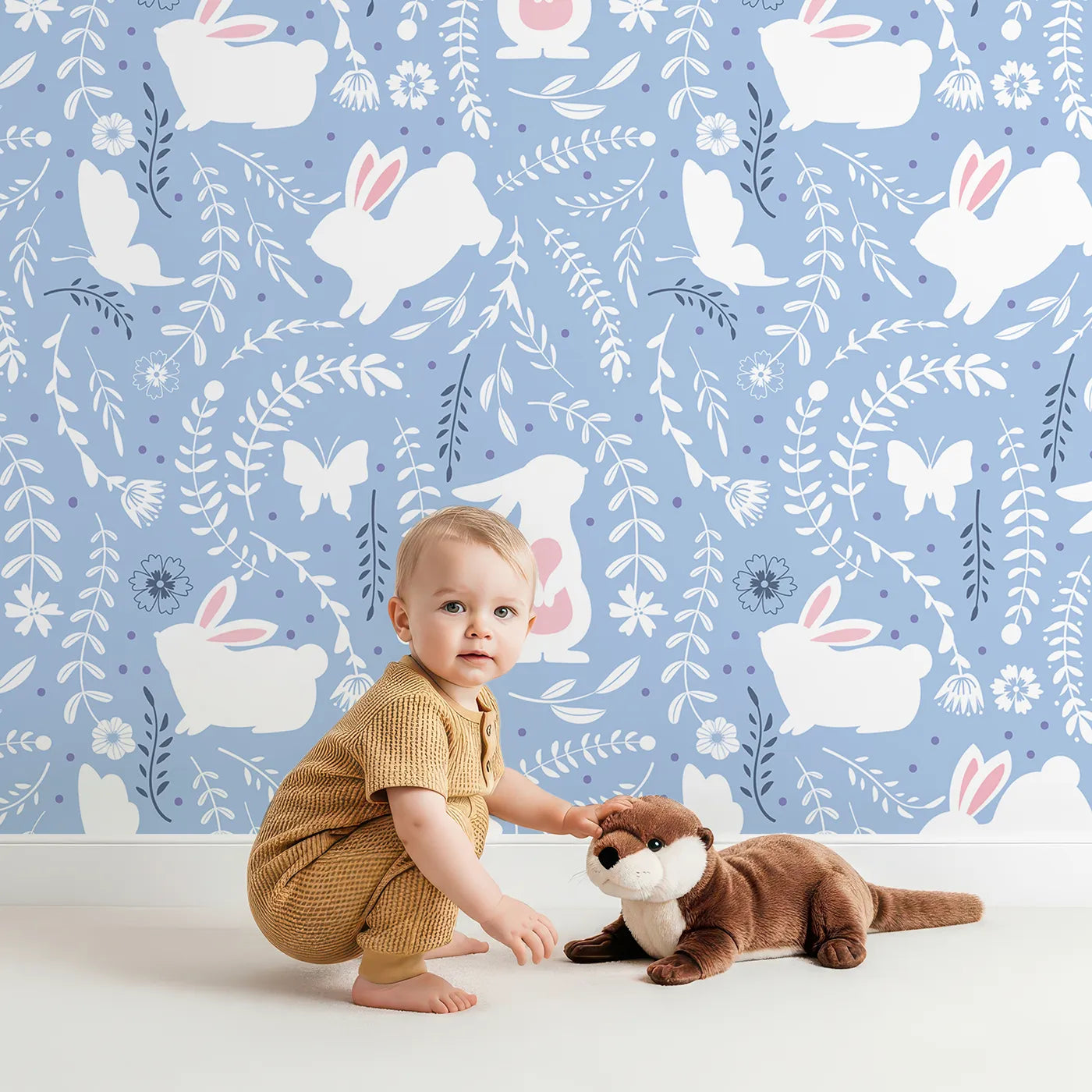 Lovely child standing in front of Whimsy Tots Bunny Hideaway Meadow Wallpaper in Bluebell with rabbit, butterfly, flower, vine in design.