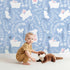 Lovely child standing in front of Whimsy Tots Bunny Hideaway Meadow Wallpaper in Bluebell with rabbit, butterfly, flower, vine in design. Lovely child standing in front of Whimsy Tots Bunny Hideaway Meadow Wallpaper in Bluebell with rabbit, butterfly, flower, vine in design.