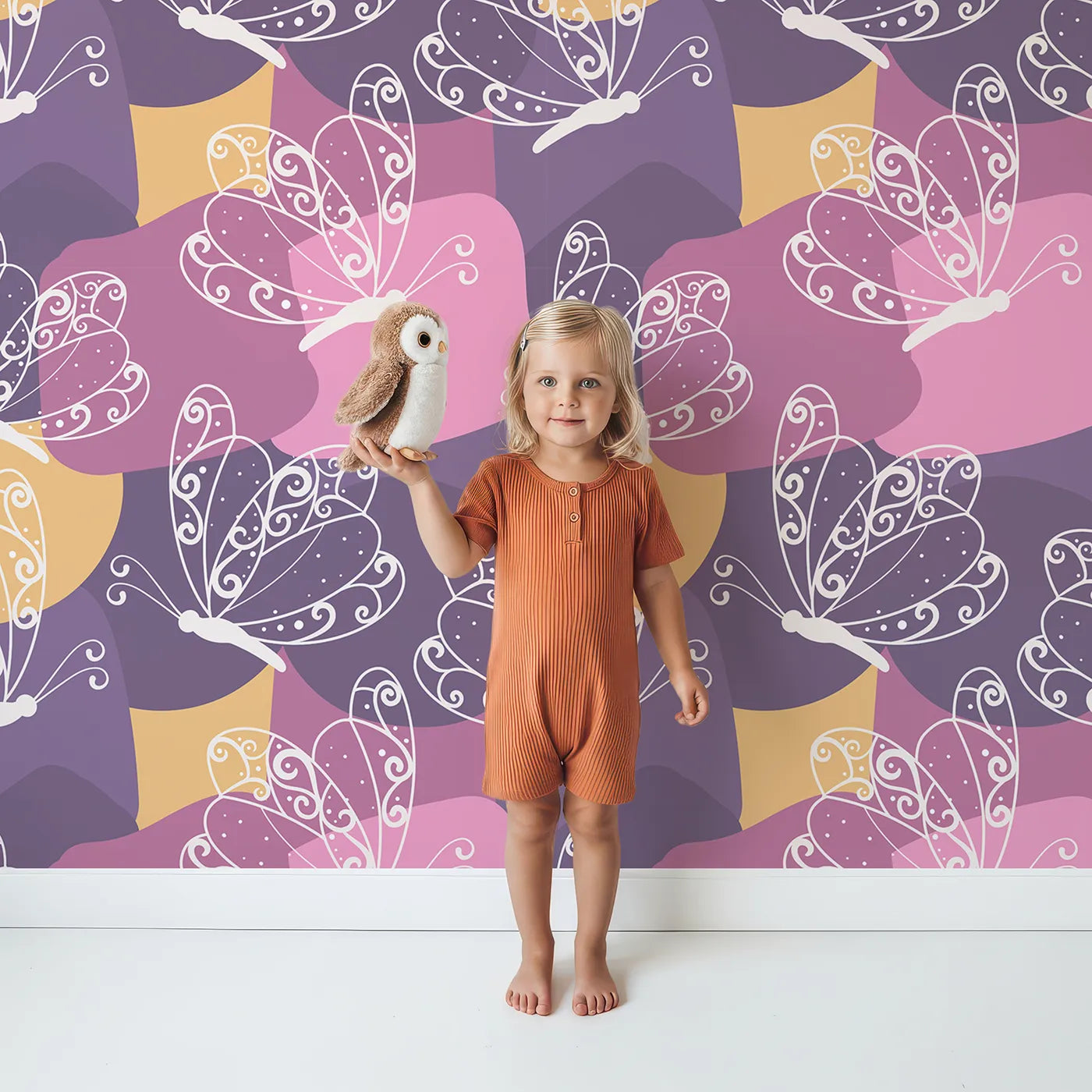 Lovely child standing in front of Whimsy Tots Flutter Dance Butterfly Wallpaper in Purple Mix with butterfly, swirl, wing, abstract shape in design.