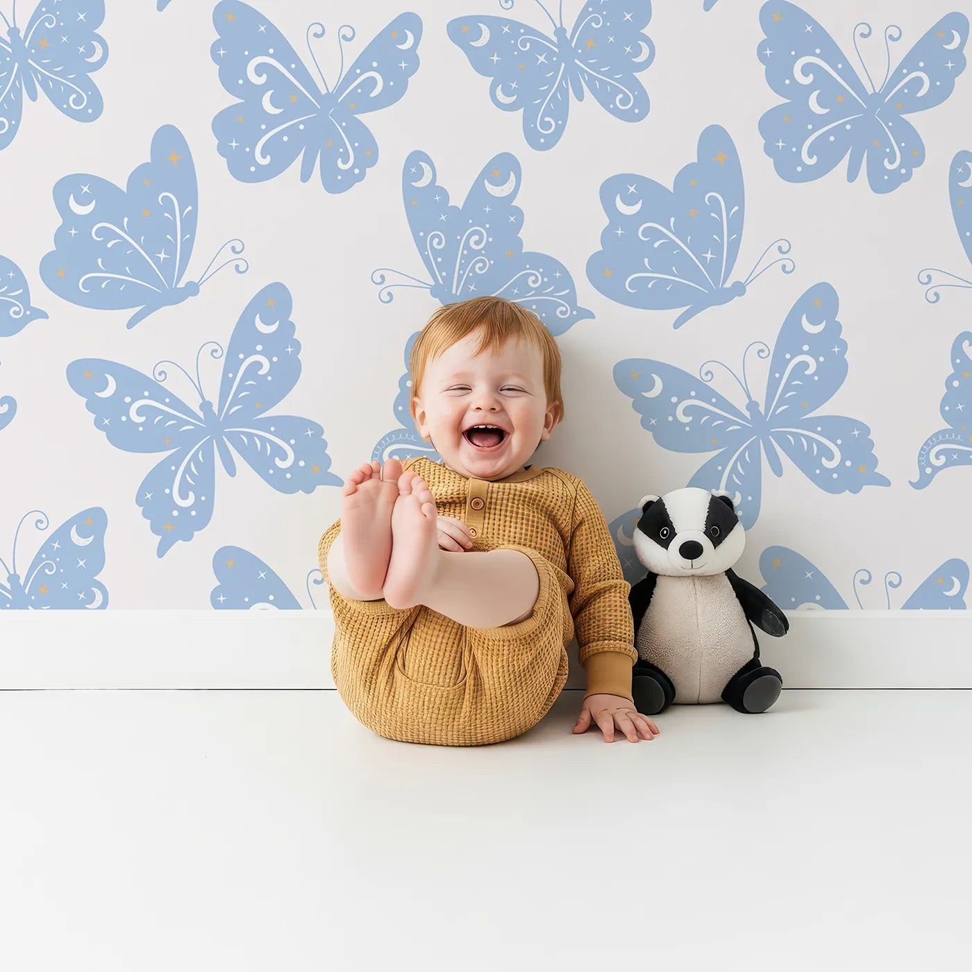 Lovely child standing in front of Whimsy Tots Celestial Wings Butterfly Wallpaper in Baby Blue with butterfly, moon, star, swirl in design.