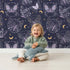 Lovely child standing in front of Whimsy Tots Starglow Garden Butterfly Wallpaper in Midnight Navy Blue with butterfly in design. Lovely child standing in front of Whimsy Tots Starglow Garden Butterfly Wallpaper in Midnight Navy Blue with butterfly in design.