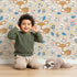Lovely child standing in front of Whimsy Tots Meadow Cuddles Deer Wallpaper in Petal Pink with deer, flower, leaf, blossom in design. Lovely child standing in front of Whimsy Tots Meadow Cuddles Deer Wallpaper in Petal Pink with deer, flower, leaf, blossom in design.
