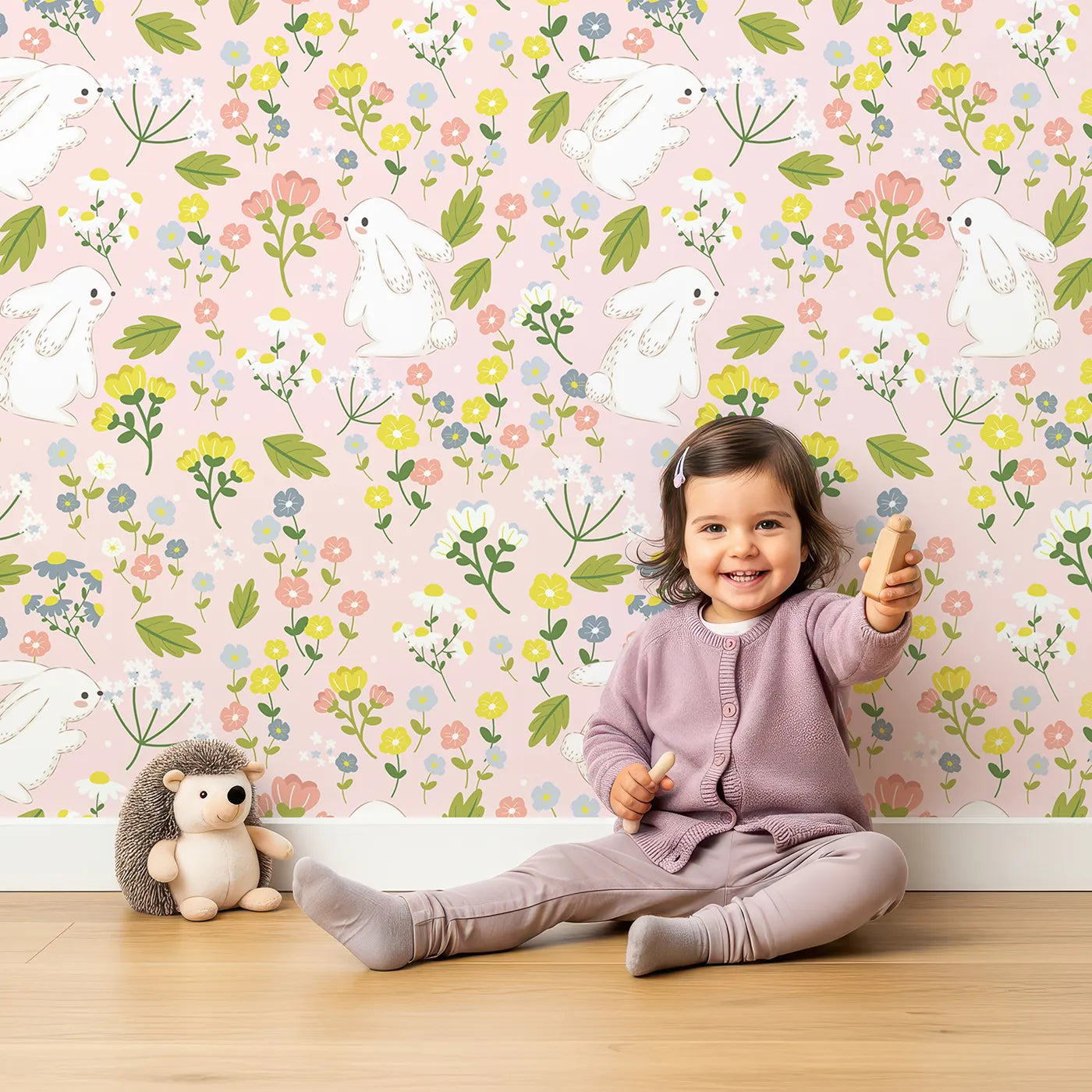 Lovely child standing in front of Whimsy Tots Bloomy Bunny Meadow Wallpaper in Petal Pink with rabbit, flower, leaf, blossom in design.
