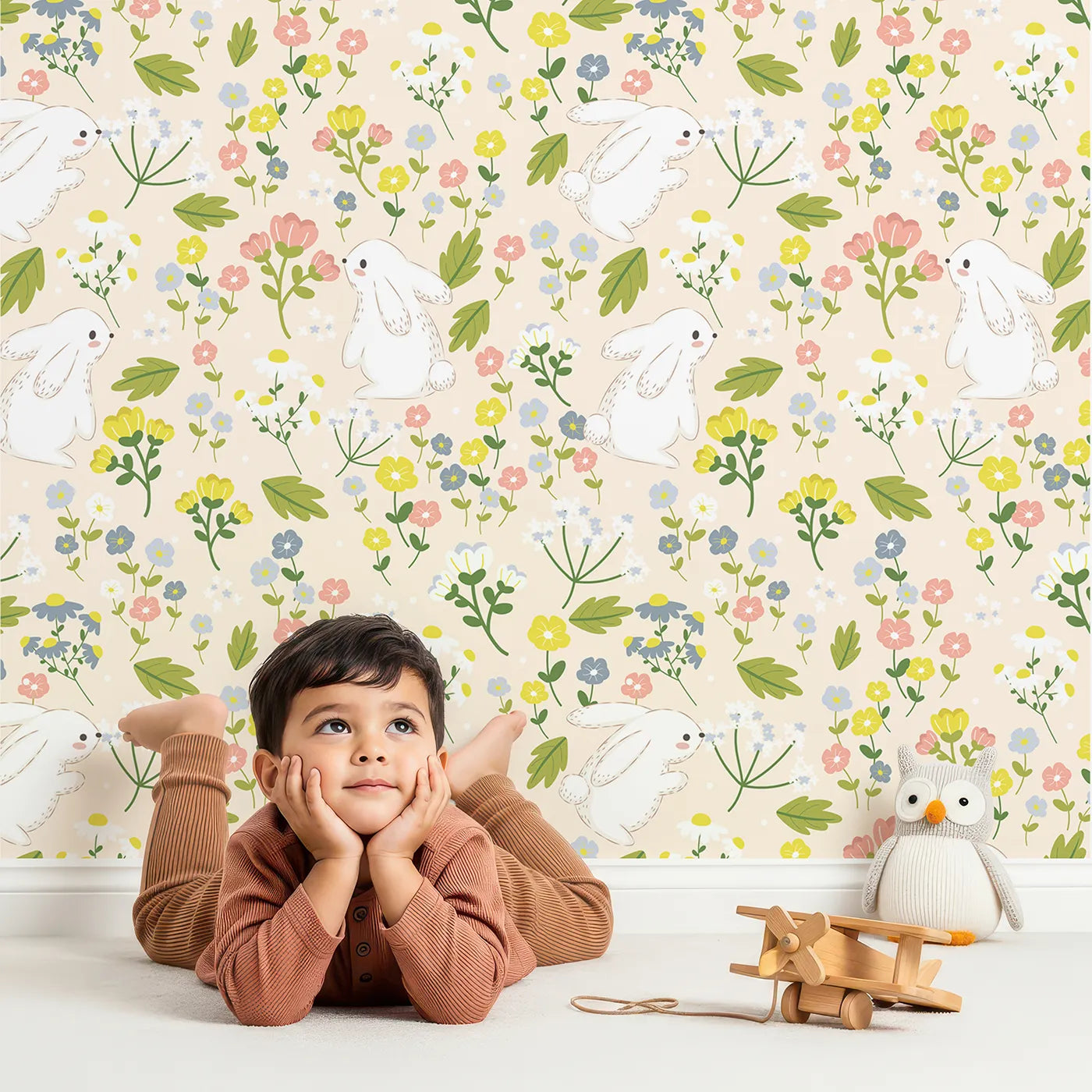 Lovely child standing in front of Whimsy Tots Bloomy Bunny Meadow Wallpaper in Oat Beige with rabbit, flower, leaf, blossom in design.