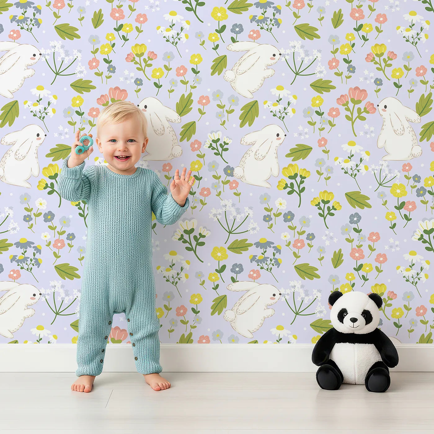 Lovely child standing in front of Whimsy Tots Bloomy Bunny Meadow Wallpaper in Lavender Mist with rabbit, flower, leaf, blossom in design.