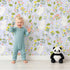 Lovely child standing in front of Whimsy Tots Bloomy Bunny Meadow Wallpaper in Lavender Mist with rabbit, flower, leaf, blossom in design. Lovely child standing in front of Whimsy Tots Bloomy Bunny Meadow Wallpaper in Lavender Mist with rabbit, flower, leaf, blossom in design.