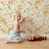 Lovely child standing in front of Whimsy Tots Spring Fawn Dance Wallpaper in Buttercream with deer, flower, meadow, tulip in design. Lovely child standing in front of Whimsy Tots Spring Fawn Dance Wallpaper in Buttercream with deer, flower, meadow, tulip in design.