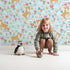 Lovely child standing in front of Whimsy Tots Spring Fawn Dance Wallpaper in Sky Blue with deer, flower, meadow, tulip in design. Lovely child standing in front of Whimsy Tots Spring Fawn Dance Wallpaper in Sky Blue with deer, flower, meadow, tulip in design.