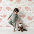 Lovely child standing in front of Whimsy Tots Tweetheart Meadow Wallpaper in Blush Pink with bird, leaf, flower, berry in design. Lovely child standing in front of Whimsy Tots Tweetheart Meadow Wallpaper in Blush Pink with bird, leaf, flower, berry in design.
