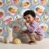 Lovely child standing in front of Whimsy Tots Garden Songbird Parade Wallpaper in Blue with bird, branch, leaf, berry in design. Lovely child standing in front of Whimsy Tots Garden Songbird Parade Wallpaper in Blue with bird, branch, leaf, berry in design.