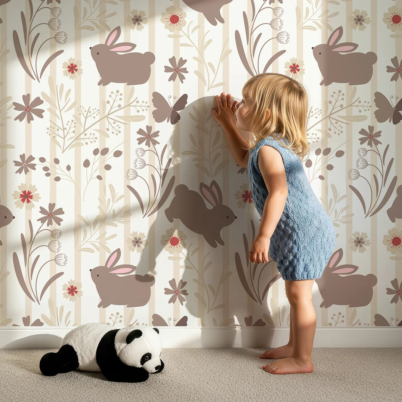 Lovely child standing in front of Whimsy Tots Meadow Hop Bunnies Wallpaper in Cream with rabbit, flower, bunny, leaf, stripe in design.