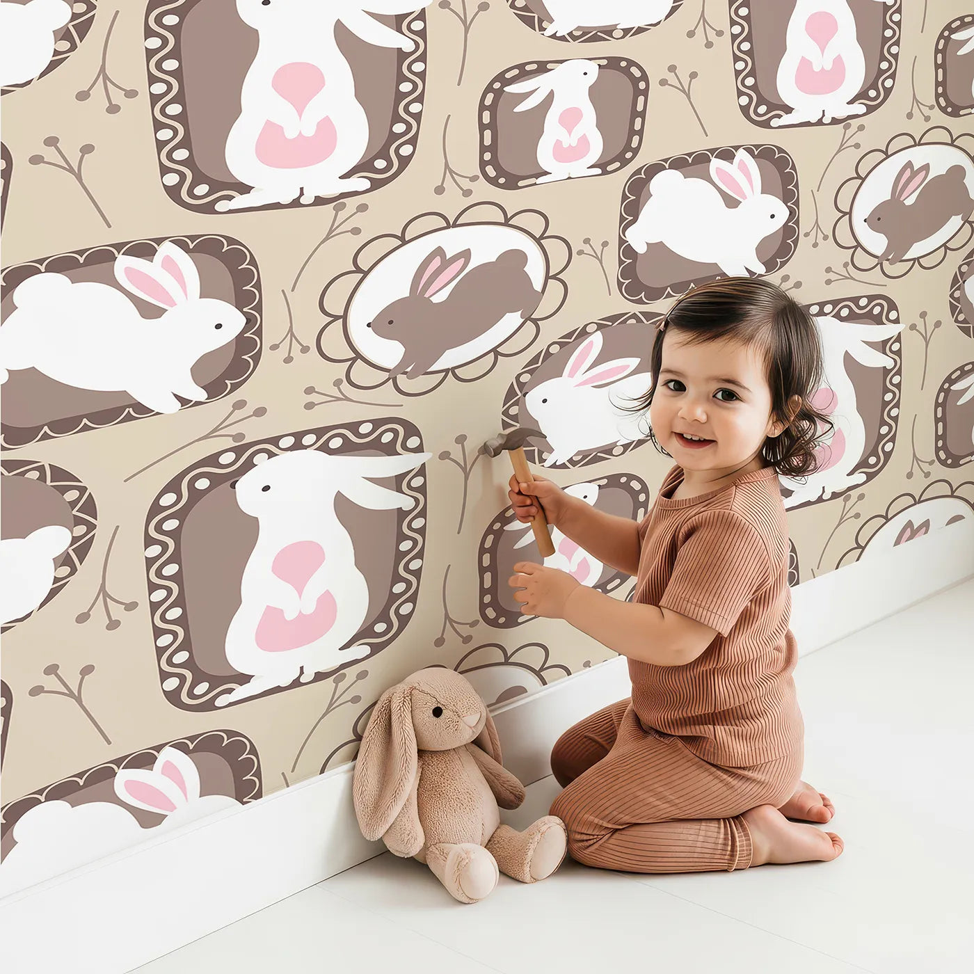 Lovely child standing in front of Whimsy Tots Framed Bunny Whimsy Wallpaper in Beige with rabbit, frame, bunny, flower, twig in design.