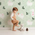 Lovely child standing in front of Whimsy Tots Bunny and Butterfly Meadow Wallpaper in Mint Green with rabbit, butterfly, bunny, branch, leaf in design. Lovely child standing in front of Whimsy Tots Bunny and Butterfly Meadow Wallpaper in Mint Green with rabbit, butterfly, bunny, branch, leaf in design.