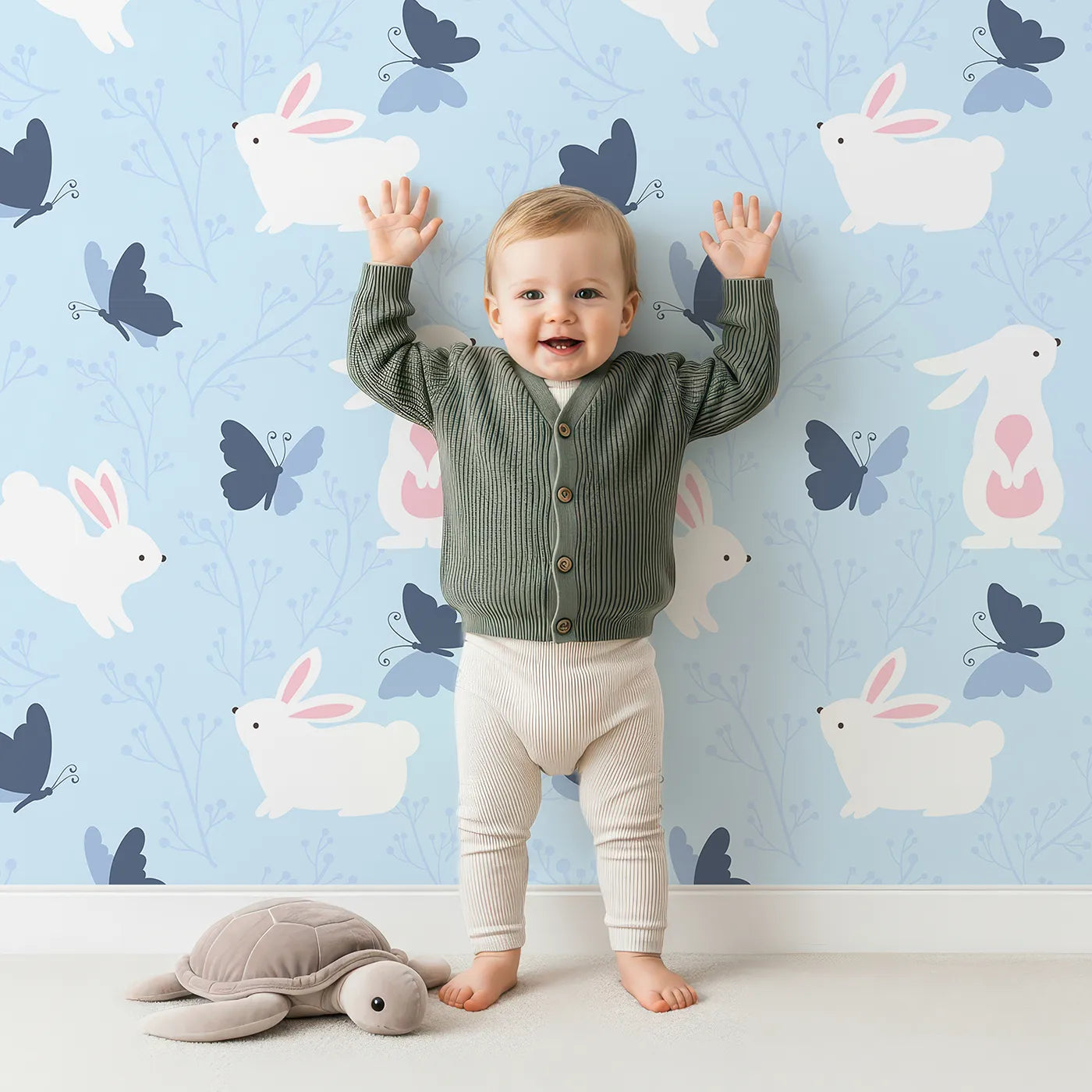 Lovely child standing in front of Whimsy Tots Bunny and Butterfly Meadow Wallpaper in Blue with rabbit, butterfly, bunny, branch, leaf in design.