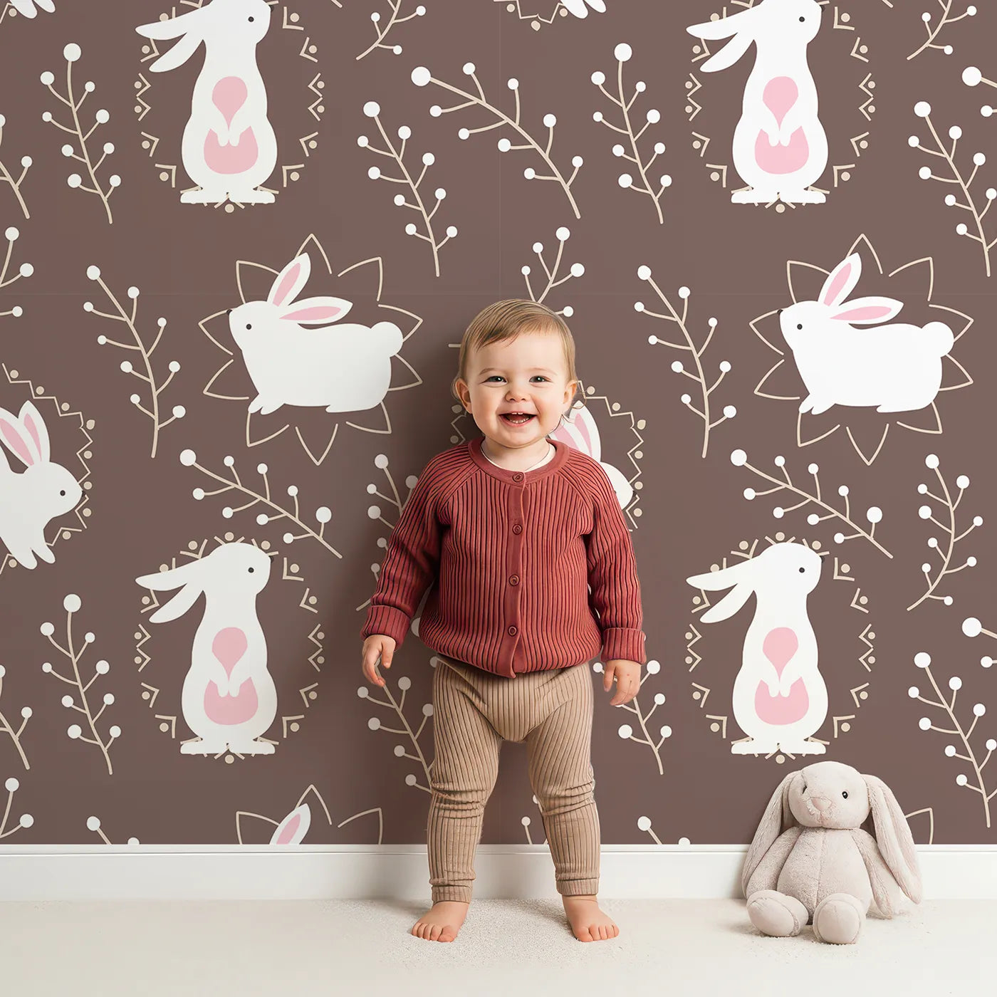 Lovely child standing in front of Whimsy Tots Tribal Bunny Sprigs Wallpaper in Cocoa Brown with rabbit, bunny, sprig, leaf, tribal motif in design.