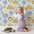 Lovely child standing in front of Whimsy Tots Jurassic Forest Friends Wallpaper in Mint Green with dinosaur, tree, triangle, dino, forest in design. Lovely child standing in front of Whimsy Tots Jurassic Forest Friends Wallpaper in Mint Green with dinosaur, tree, triangle, dino, forest in design.