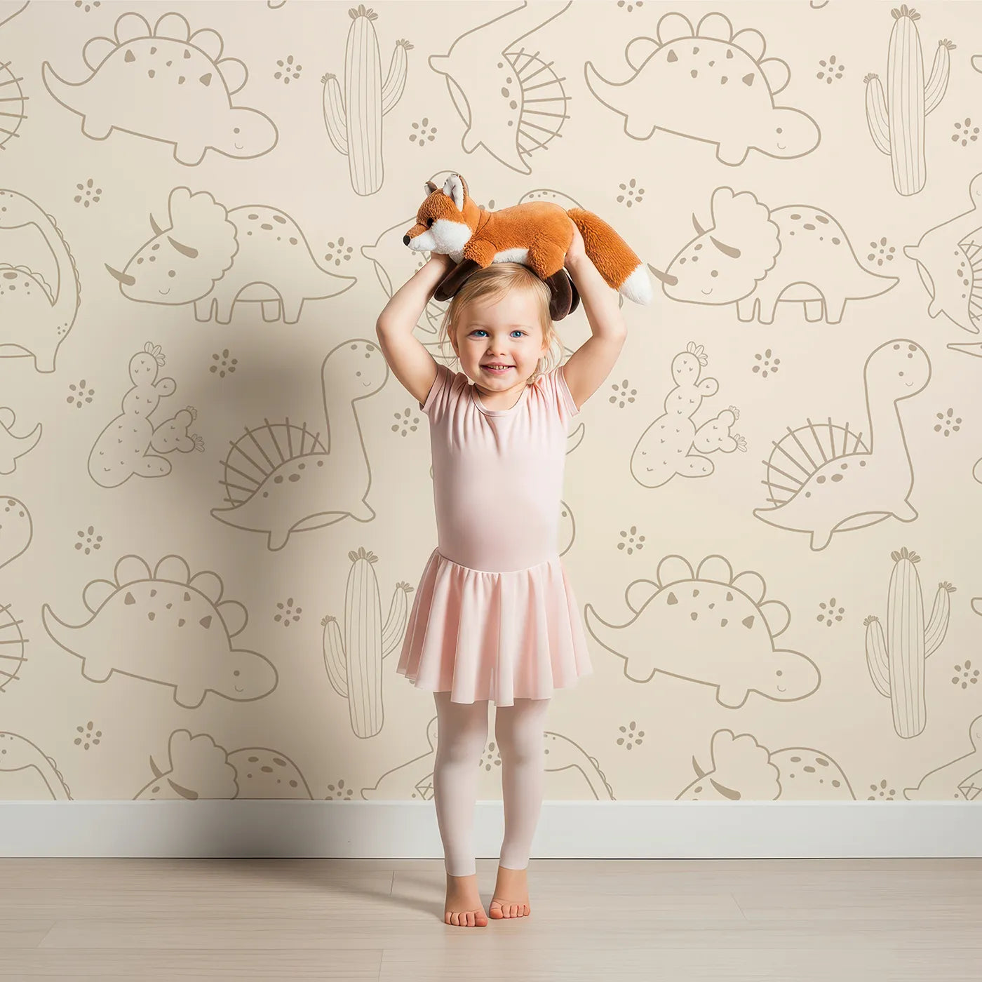 Lovely child standing in front of Whimsy Tots Desert Dino Parade Wallpaper in Sand with dinosaur, cactus, flower in design.