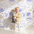 Lovely child standing in front of Whimsy Tots Cactus Canyon Dinos Wallpaper in Lilac Lavender with dinosaur, cactus, rock, spike in design. Lovely child standing in front of Whimsy Tots Cactus Canyon Dinos Wallpaper in Lilac Lavender with dinosaur, cactus, rock, spike in design.