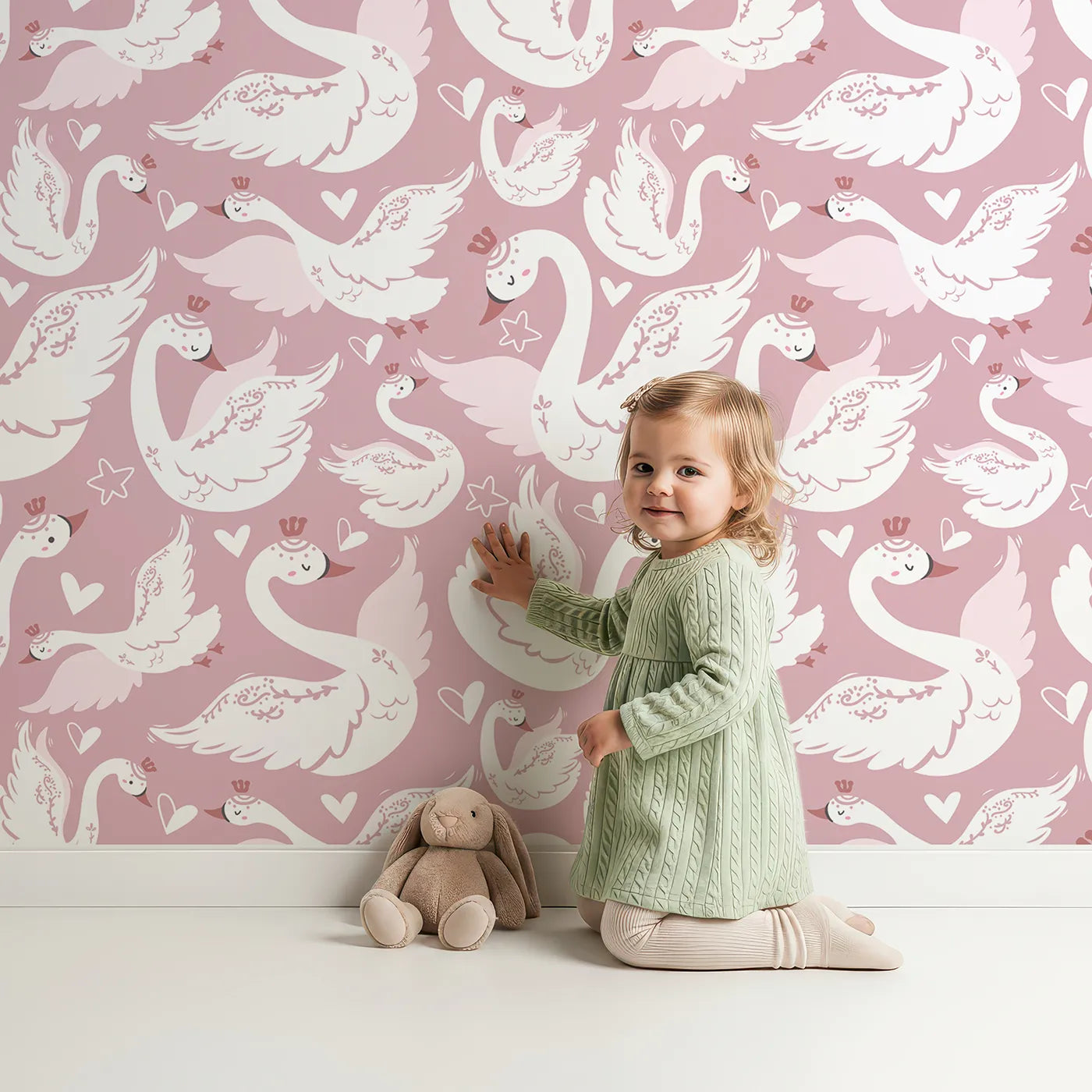 Lovely child standing in front of Whimsy Tots Swan Princess Waltz Wallpaper in Blush Pink with swan, crown, wing, heart, star in design.