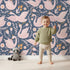 Lovely child standing in front of Whimsy Tots Starlit Swan Ballet Wallpaper in Navy Blue with swan, crown, flower, bow, leaf in design. Lovely child standing in front of Whimsy Tots Starlit Swan Ballet Wallpaper in Navy Blue with swan, crown, flower, bow, leaf in design.