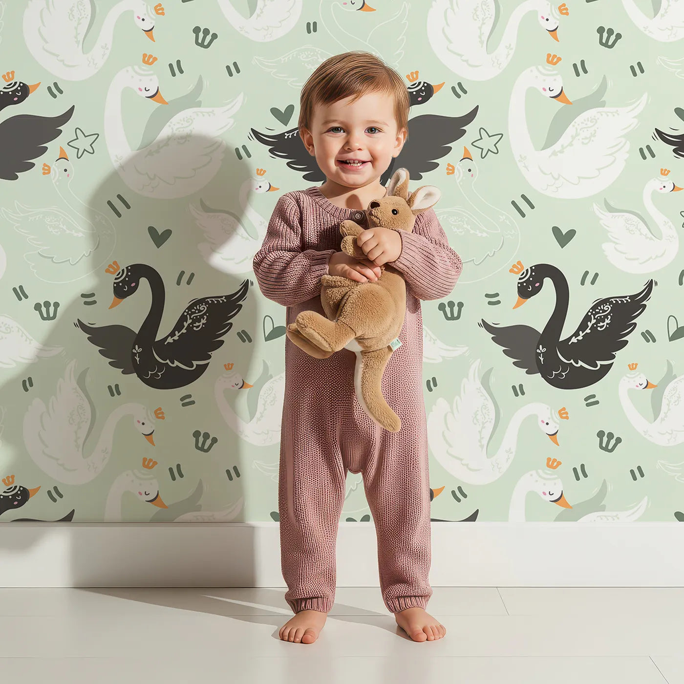 Lovely child standing in front of Whimsy Tots Royal Swan Parade Wallpaper in Mint Green with swan, crown, heart, star, wing in design.
