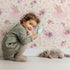 Lovely child standing in front of Whimsy Tots Blooming Swan Garden Wallpaper in Cream with swan, flower, crown, tulip, ripple in design. Lovely child standing in front of Whimsy Tots Blooming Swan Garden Wallpaper in Cream with swan, flower, crown, tulip, ripple in design.