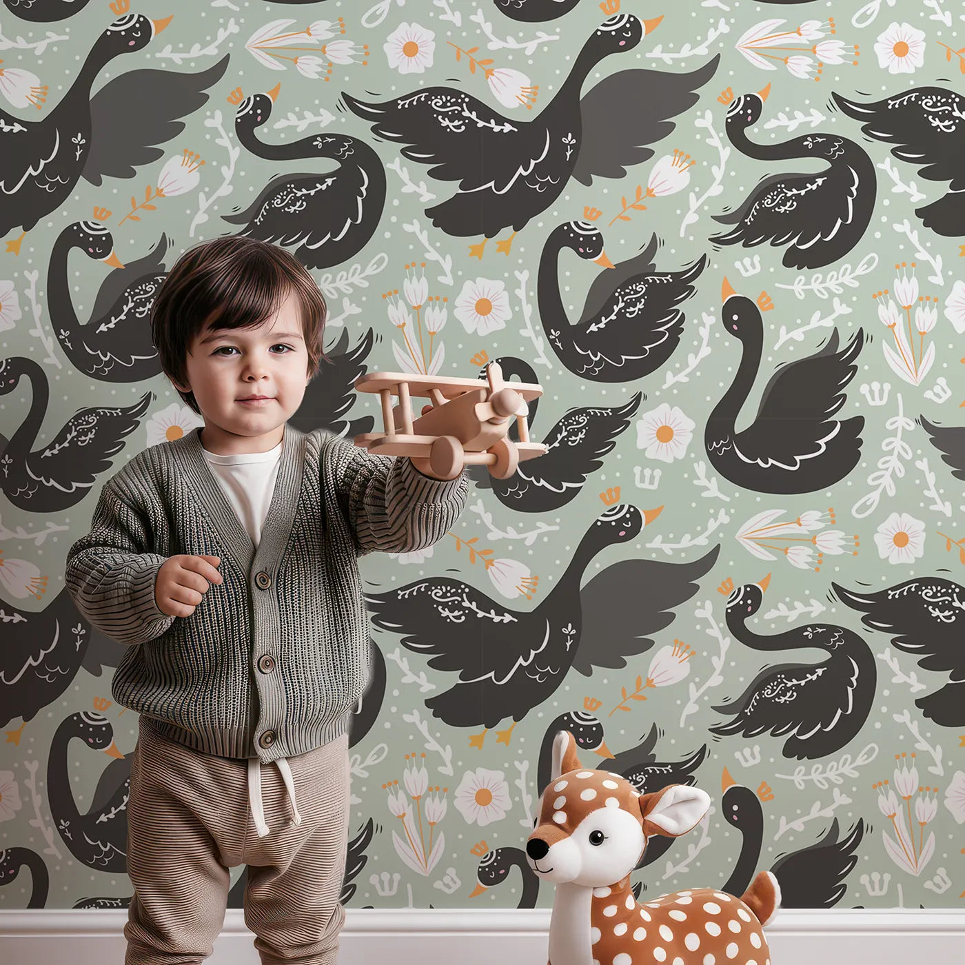 Lovely child standing in front of Whimsy Tots Regal Swan Parade Wallpaper in Sage Green with swan, flower, crown, leaf in design.