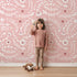 Lovely child standing in front of Whimsy Tots Spring Meadow Whispers Wallpaper in Blush Pink with flower, vine, leaf, dot in design. Lovely child standing in front of Whimsy Tots Spring Meadow Whispers Wallpaper in Blush Pink with flower, vine, leaf, dot in design.