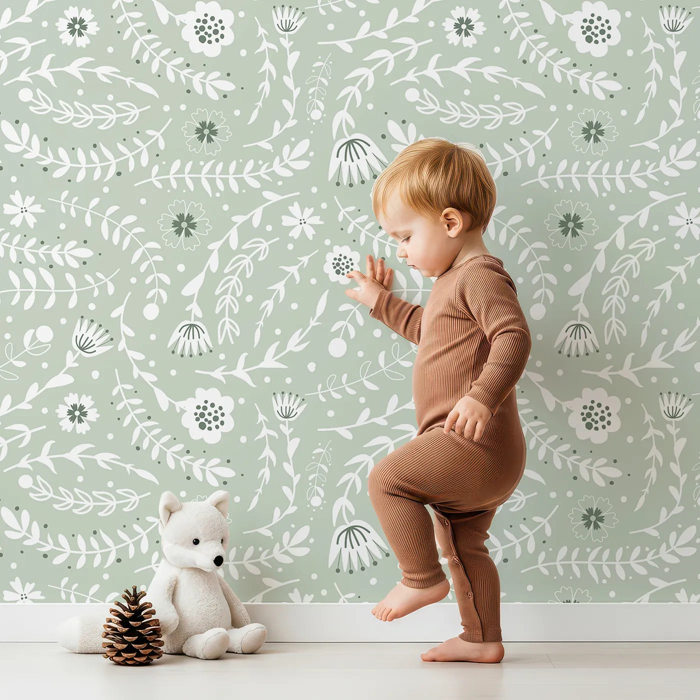 Lovely child standing in front of Whimsy Tots Spring Meadow Whispers Wallpaper in Sage Green with flower, vine, leaf, dot in design.