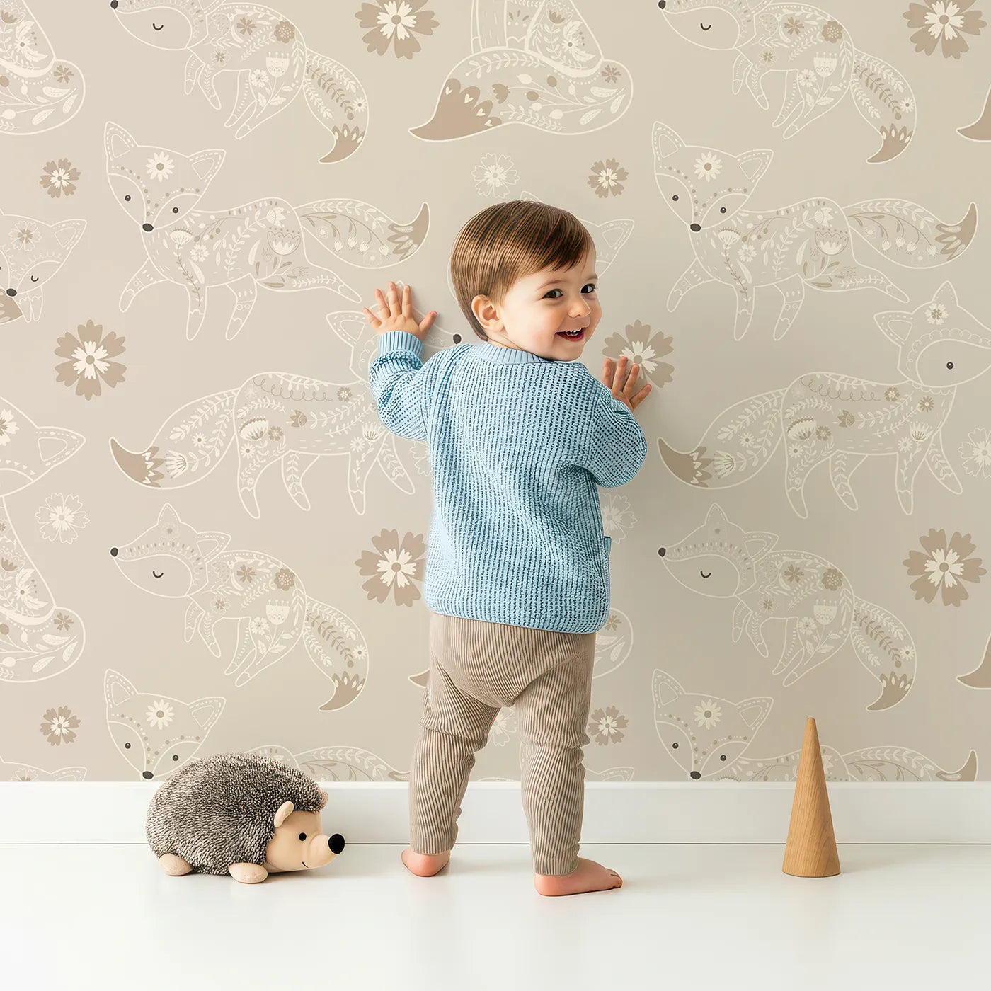 Lovely child standing in front of Whimsy Tots Floral Fox Cuddles Wallpaper in Taupe Beige with fox, flower, leaf in design.