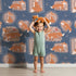 Lovely child standing in front of Whimsy Tots Fox Meadow Moments Wallpaper in Midnight Blue with fox, flower, frame in design. Lovely child standing in front of Whimsy Tots Fox Meadow Moments Wallpaper in Midnight Blue with fox, flower, frame in design.