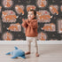 Lovely child standing in front of Whimsy Tots Fox Meadow Moments Wallpaper in Charcoal Gray with fox, flower, frame in design. Lovely child standing in front of Whimsy Tots Fox Meadow Moments Wallpaper in Charcoal Gray with fox, flower, frame in design.