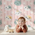 Lovely child standing in front of Whimsy Tots Pawprint Kitty Parade Wallpaper in Blush Pink with cat, pawprint, stripe in design. Lovely child standing in front of Whimsy Tots Pawprint Kitty Parade Wallpaper in Blush Pink with cat, pawprint, stripe in design.