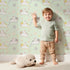 Lovely child standing in front of Whimsy Tots Cozy Pawstep Kittens Wallpaper in Mint Green with cat, kitten, pawprint, spot in design. Lovely child standing in front of Whimsy Tots Cozy Pawstep Kittens Wallpaper in Mint Green with cat, kitten, pawprint, spot in design.