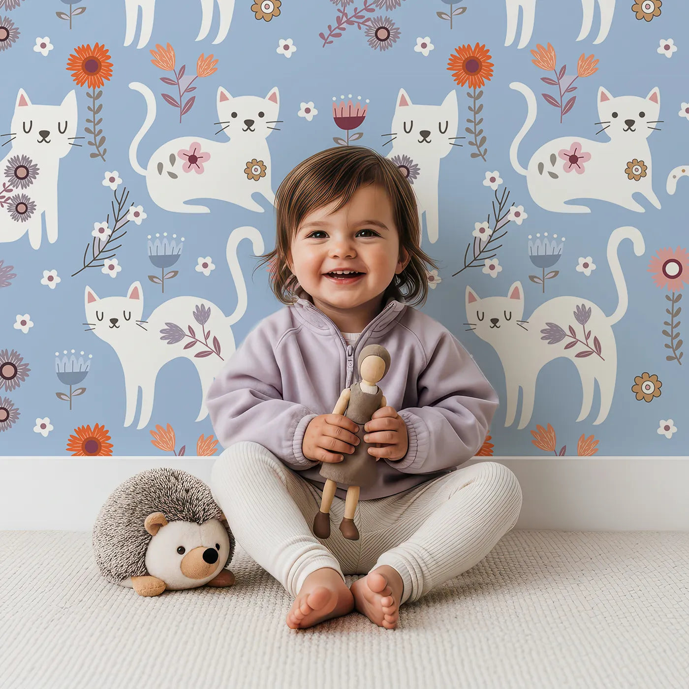 Lovely child standing in front of Whimsy Tots Floral Kitty Parade Wallpaper in Sky Blue with cat, flower, kitten, daisy in design.