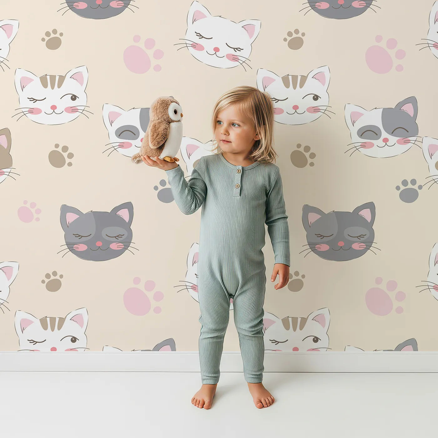 Lovely child standing in front of Whimsy Tots Whisker Wink Kitty Wallpaper in Beige with cat, pawprint, whisker, smile in design.