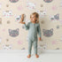 Lovely child standing in front of Whimsy Tots Whisker Wink Kitty Wallpaper in Beige with cat, pawprint, whisker, smile in design. Lovely child standing in front of Whimsy Tots Whisker Wink Kitty Wallpaper in Beige with cat, pawprint, whisker, smile in design.