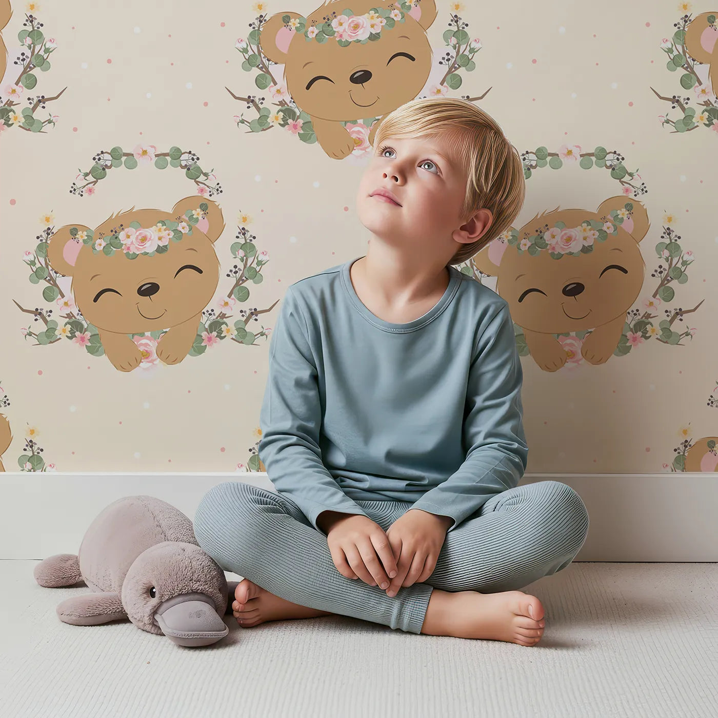 Lovely child standing in front of Whimsy Tots Floral Bear Hugs Wallpaper in Soft Cream with bear, flower, crown, branch, leaf in design.
