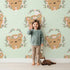 Lovely child standing in front of Whimsy Tots Floral Bear Hugs Wallpaper in Mint Green with bear, flower, crown, branch, leaf in design. Lovely child standing in front of Whimsy Tots Floral Bear Hugs Wallpaper in Mint Green with bear, flower, crown, branch, leaf in design.
