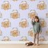 Lovely child standing in front of Whimsy Tots Floral Bear Hugs Wallpaper in Lavender Mist with bear, flower, crown, branch, leaf in design. Lovely child standing in front of Whimsy Tots Floral Bear Hugs Wallpaper in Lavender Mist with bear, flower, crown, branch, leaf in design.