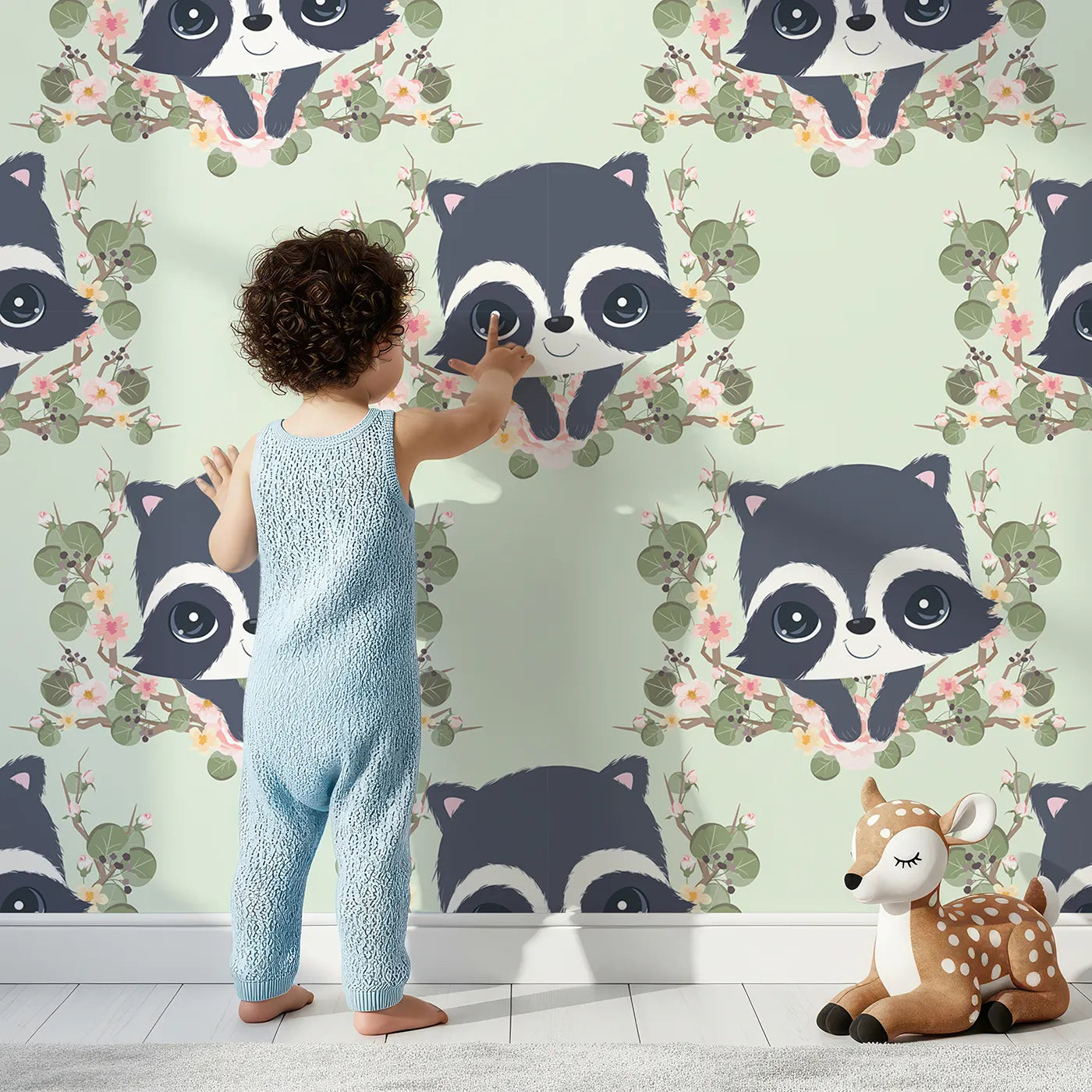 Lovely child standing in front of Whimsy Tots Floral Raccoon Peek Wallpaper in Mint Green with raccoon, flower, crown, leaf, branch in design.