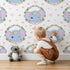 Lovely child standing in front of Whimsy Tots Floral Elephant Wink Wallpaper in Sweetheart Pink with elephant, heart, flower, crown, branch, leaf in design. Lovely child standing in front of Whimsy Tots Floral Elephant Wink Wallpaper in Sweetheart Pink with elephant, heart, flower, crown, branch, leaf in design.