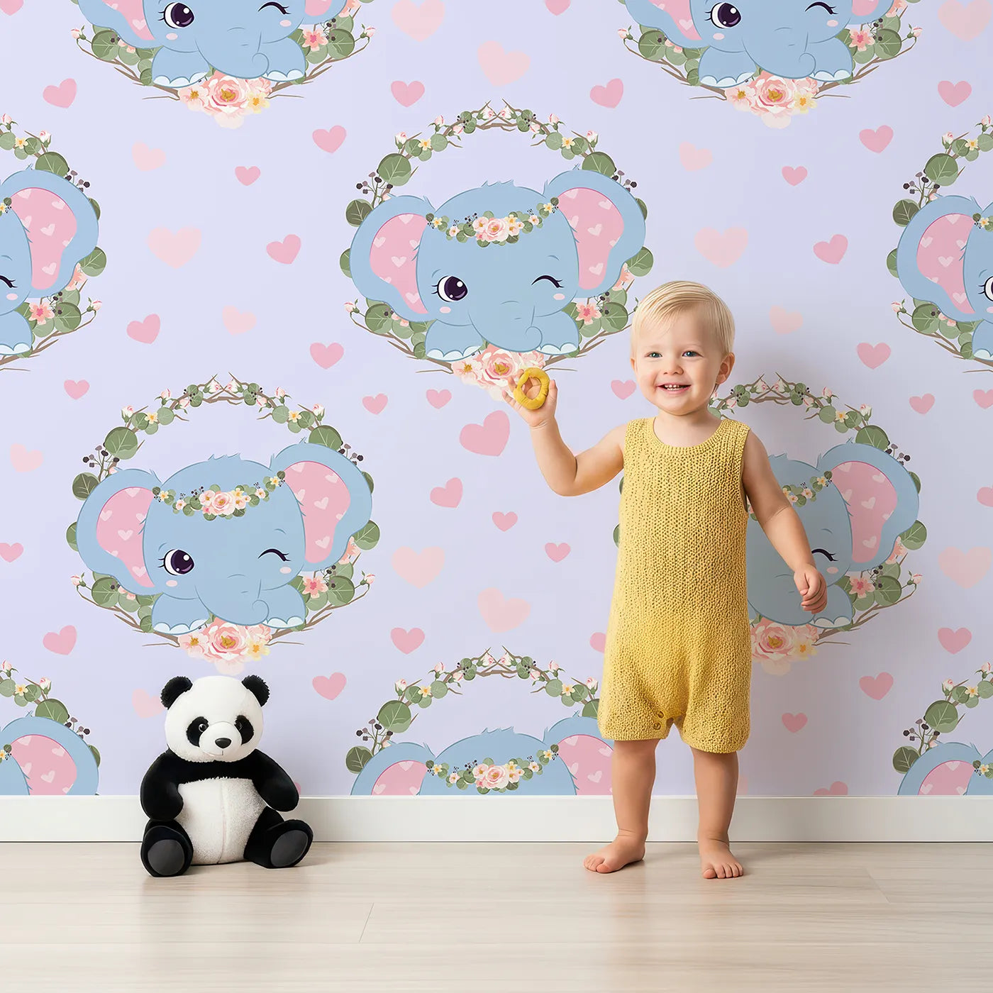 Lovely child standing in front of Whimsy Tots Floral Elephant Wink Wallpaper in Lilac Whisper Lavender with elephant, heart, flower, crown, branch, leaf in design.