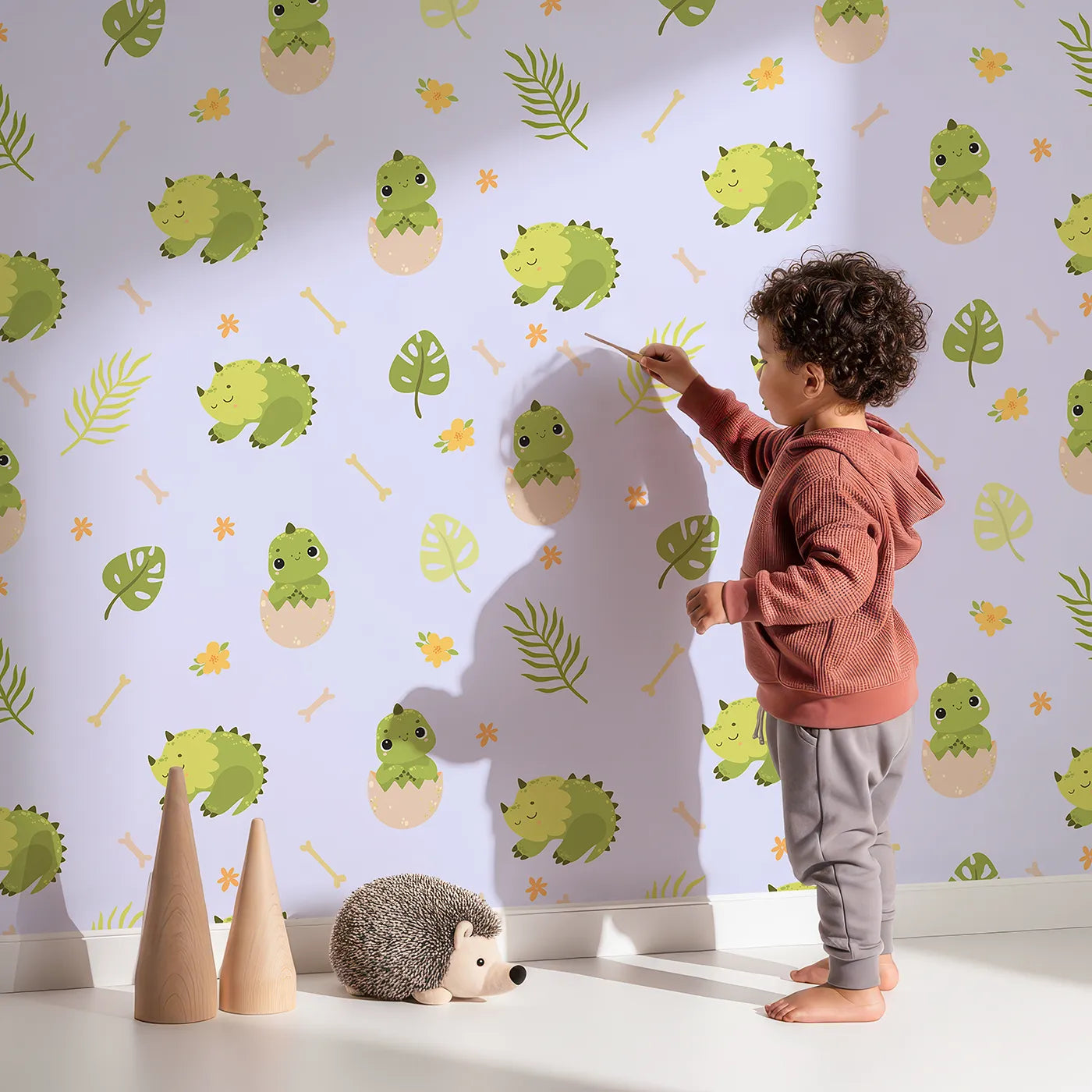 Lovely child standing in front of Whimsy Tots Hatching Dino Friends Wallpaper in Lilac Mist Lavender with dinosaur, egg, leaf, flower, bone in design.