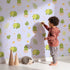 Lovely child standing in front of Whimsy Tots Hatching Dino Friends Wallpaper in Lilac Mist Lavender with dinosaur, egg, leaf, flower, bone in design. Lovely child standing in front of Whimsy Tots Hatching Dino Friends Wallpaper in Lilac Mist Lavender with dinosaur, egg, leaf, flower, bone in design.