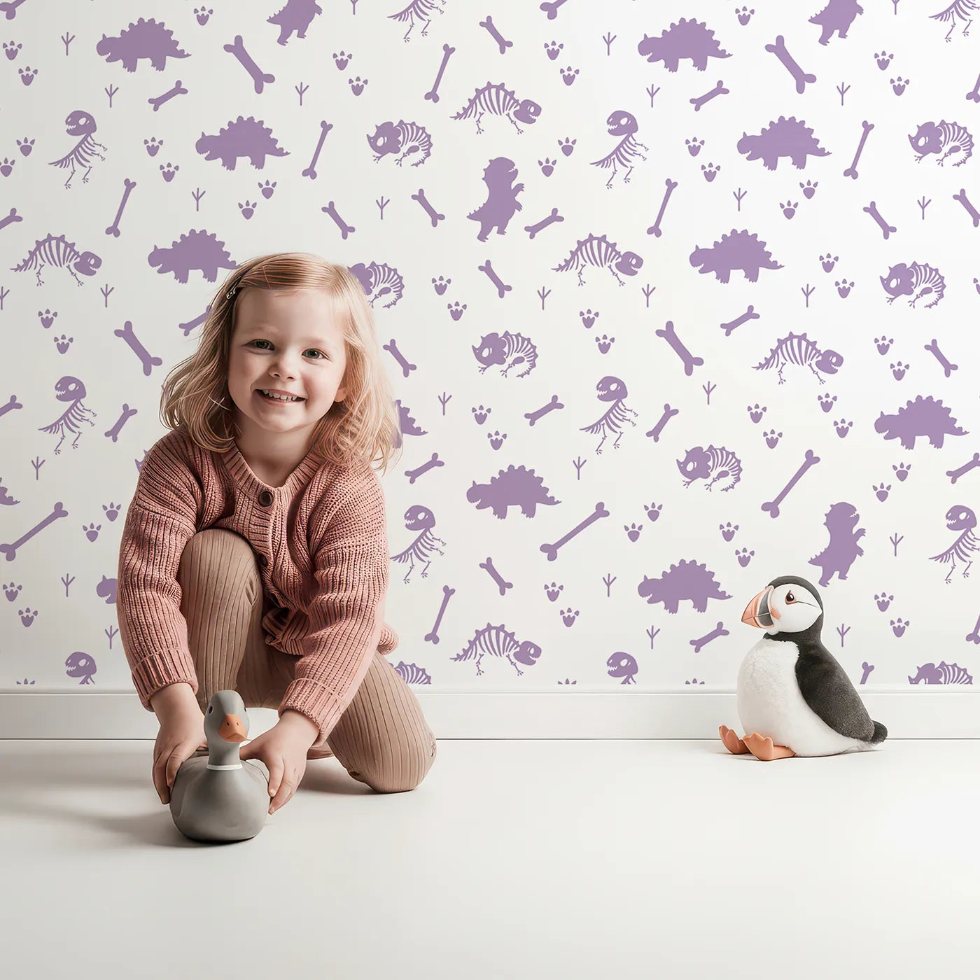Lovely child standing in front of Whimsy Tots Fossil Roar Parade Wallpaper in Lavender Bone with dinosaur, skeleton, bone, footprint in design.