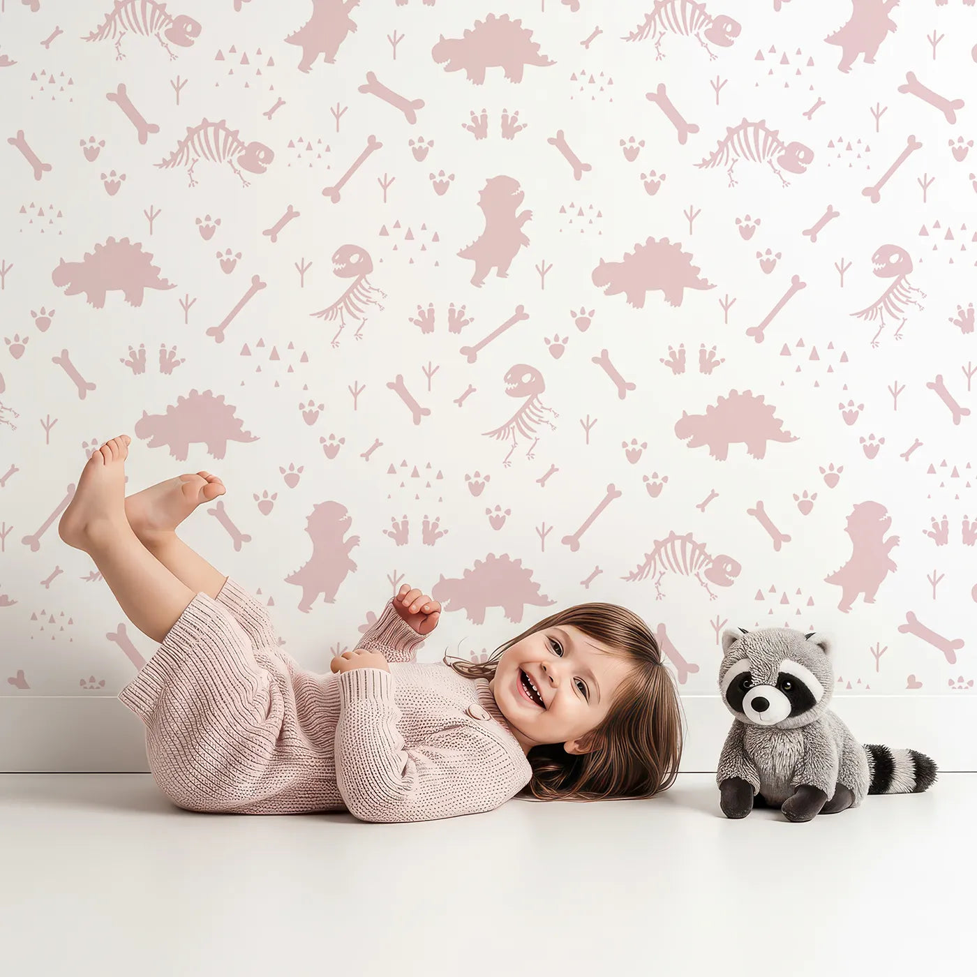 Lovely child standing in front of Whimsy Tots Dino Fossil Footprints Wallpaper in Dusty Pink with dinosaur, fossil, bone, footprint in design.